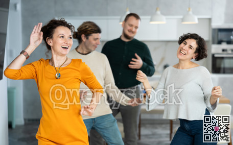 Four adult friends dancing and singing at home. Cheerful women and men enjoy music together. Happy people celebrating friendship