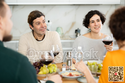 Two married couples are sitting at table, enjoying food and wine, chatting, talking, laughing.