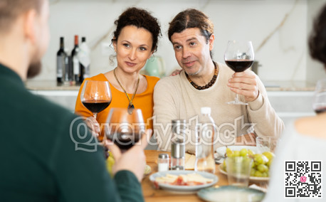 Group of joyful individuals are celebrating a holiday, enjoying drinks and conversation around table in their home