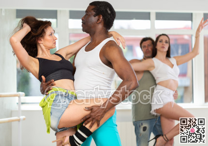 Smiling multiracial men and women enjoying partner dance while training together in studio