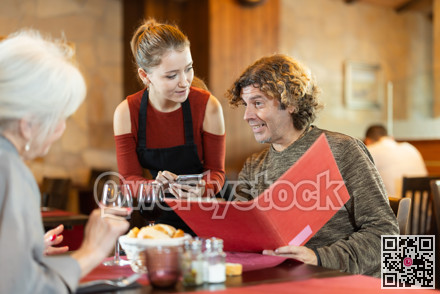 Young waitress taking order from adult couple in restaurant