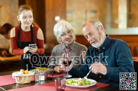 At cafe, girl waitress communicates with mature couple of customer, accepts order