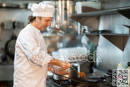 Middle-aged male cook preparing dish in restaurant kitchen