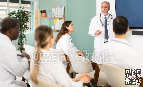 During lesson, mature male doctor with remote controller tell material, speaks to group of students