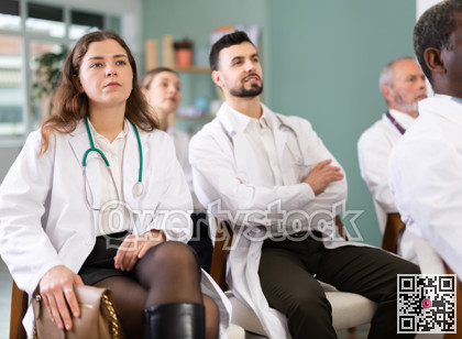 Female doctor listens to lecture with colleagues in auditorium