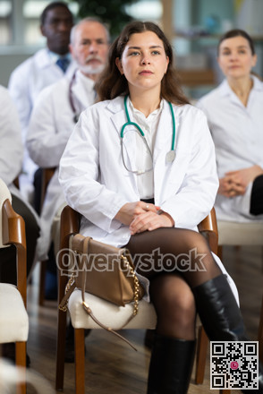 Female doctor listens to lecture with colleagues in auditorium