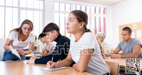 Young girl listening to lecture and taking notes in classroom
