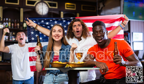 Happy multiracial sport fans holding the flag of USA, enjoing game, beer and chips in the bar