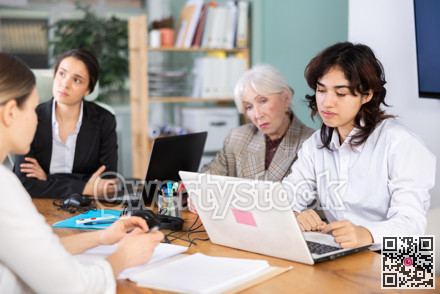 Tired Asian girl is sitting at computer at work in crowded office