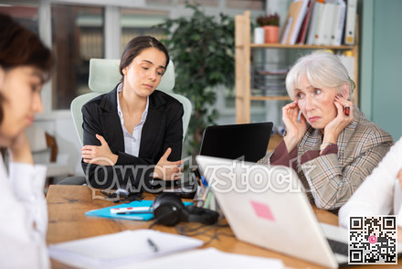 Tired mature woman is sitting at computer at work in crowded office