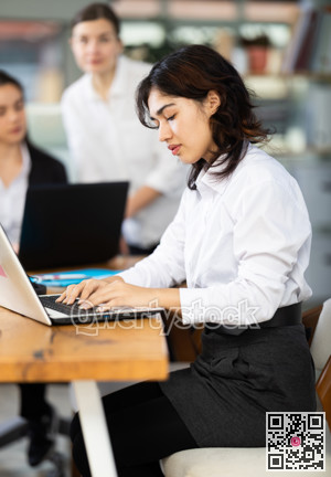 Young woman works on laptop with female colleagues