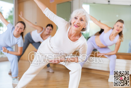 Mature female coach dancing and practicing new movements with group of young women in gym. Dance and wellbeing concept