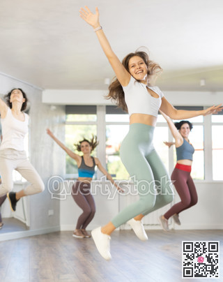 Girls engaged shake leg in dance fitness hall with friends, group of youthful people jumped into air
