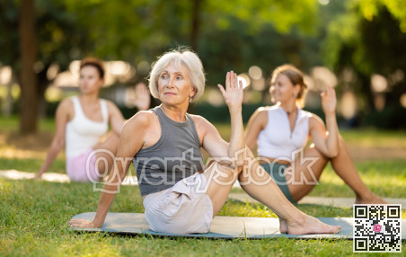 Sedulous old lady and group of women doing spinal twist pose of yoga on mat in light city park together