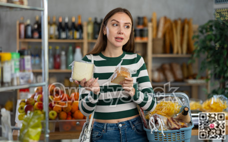 Smiling young girl with shopping basket trying to make choice holding two sorts of cheese in grocery store