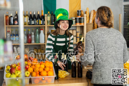 Female vendor in St. Patrick hat offers to buy male vendor traditional Irish ale