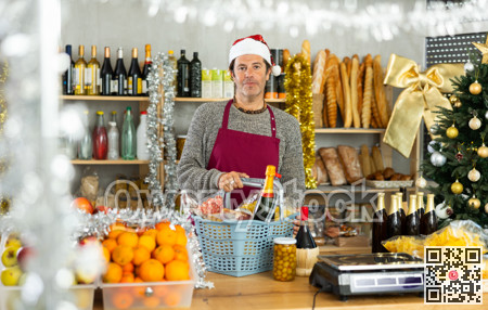 Adult male seller in grocery store posing behind counter with basket full of products for Christmas table