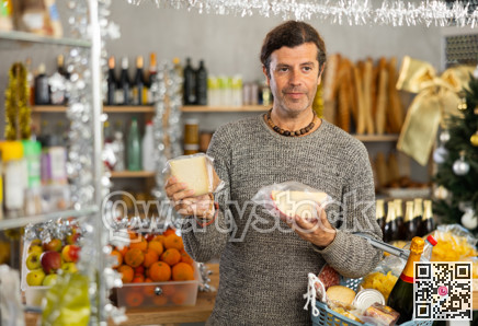 Man choosing cheese in grocery store adorned with Christmas ornaments