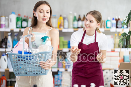 Female salesperson and customer with shopping basket choosing goods together in supermarket