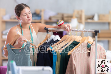 Young dressmaker taking finished dress from rack