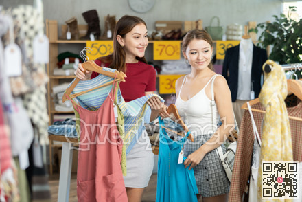 Friendly sisters choosing summer clothing in outlet store
