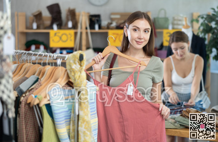 Young girl elect something summer clothing in store. Female client choosing something in background