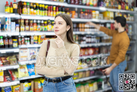 In food store, woman buyer looking for something on shelf of showcase