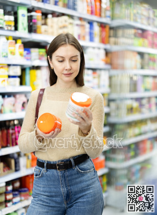 Positive woman buyers chooses shampoo or shower gel in household chemicals store