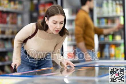 Woman standing near refrigerated display cases choosing frozen food in supermarket