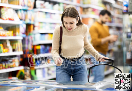 Woman standing near refrigerated display cases choosing frozen food in supermarket
