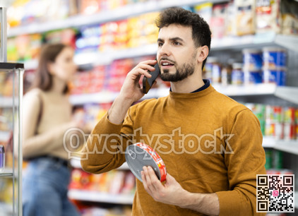 Young man choosing canned goods while talking on phone