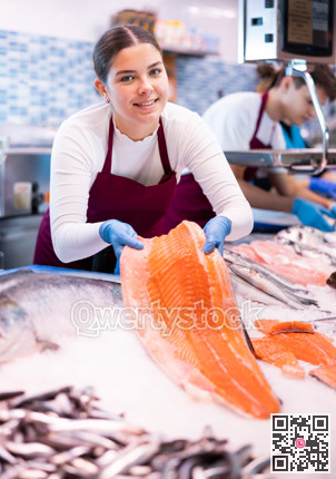 Seller in apron standing near counter offering fresh fish pink salmon