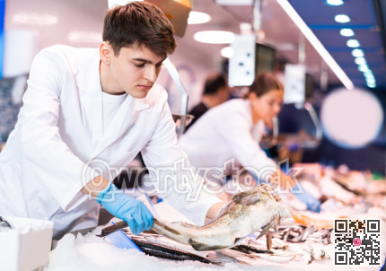Positive salesman demonstrating cod in fish store