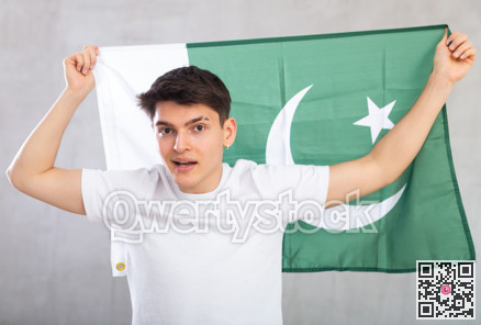 Happy young man holding flag of Pakistan against unicoloured background