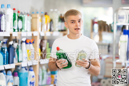 Focused young man choosing dishwashing liquid on supermarket shelf