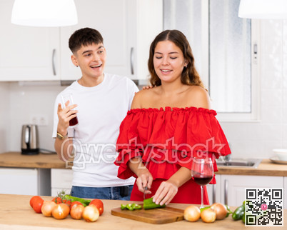 Young happy married couple with glasses of wine preparing a festive dinner