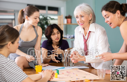 Emotional female colleagues of business company different ages playing exciting board game in office