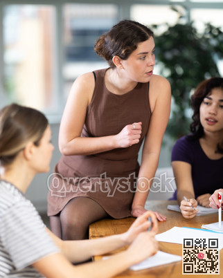 Young woman sitting on table during group discussion with diverse ladies