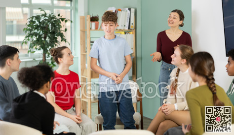 Teenage boy talking to students sitting in circle while teacher watching