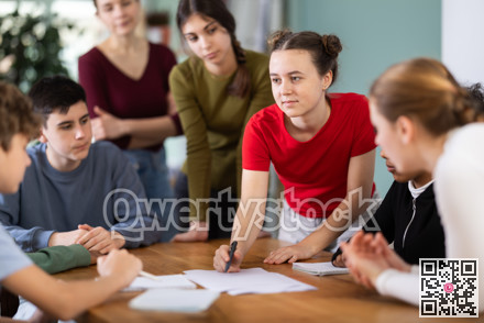 At round table meeting, teen participants discuss problem and try to find solution, teacher watching