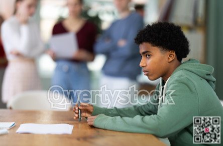 Upset young male student sitting alone at desk