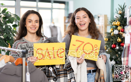 Two women holding posters of 70 percent discounts and sales in a clothing Christmas store