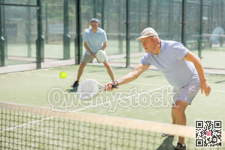 Portrait of sporty mature man playing padel on open court on autumn day, ready to hit ball. Health and active lifestyle concept