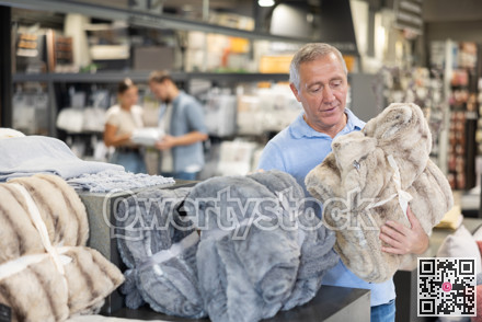 Elderly buyer carefully selects warm blanket to create coziness in his apartment