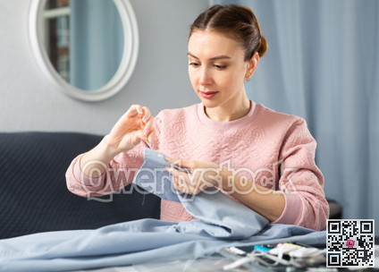 Young woman sewing on button at home