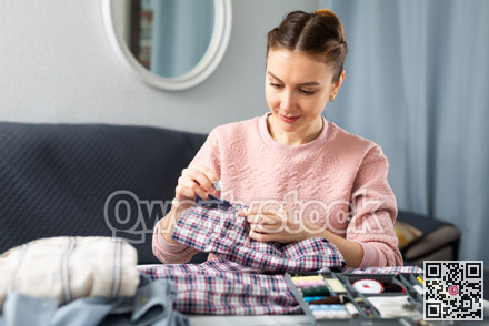 Young woman sewing on button at home