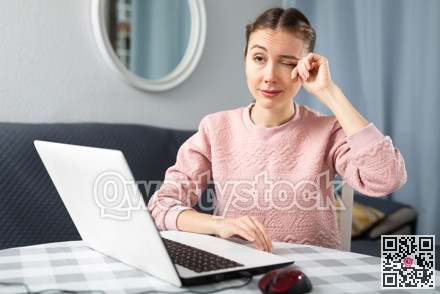 Young woman rubbing her eyes, using laptop in home office