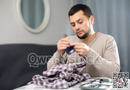 Man sewing button on shirt sleeve at home