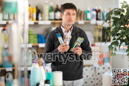 Among shop windows, man buyer leisurely examines goods and chooses toothbrush