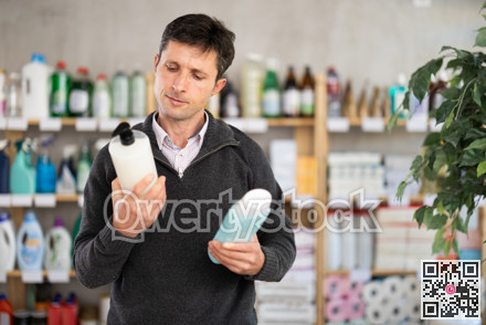 Man buyer chooses shampoo or shower gel in household goods department of supermarket